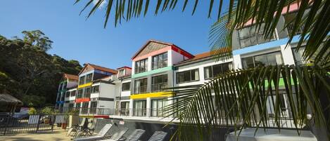 A multi-story hotel with colorful facades and a pool area with sun loungers.