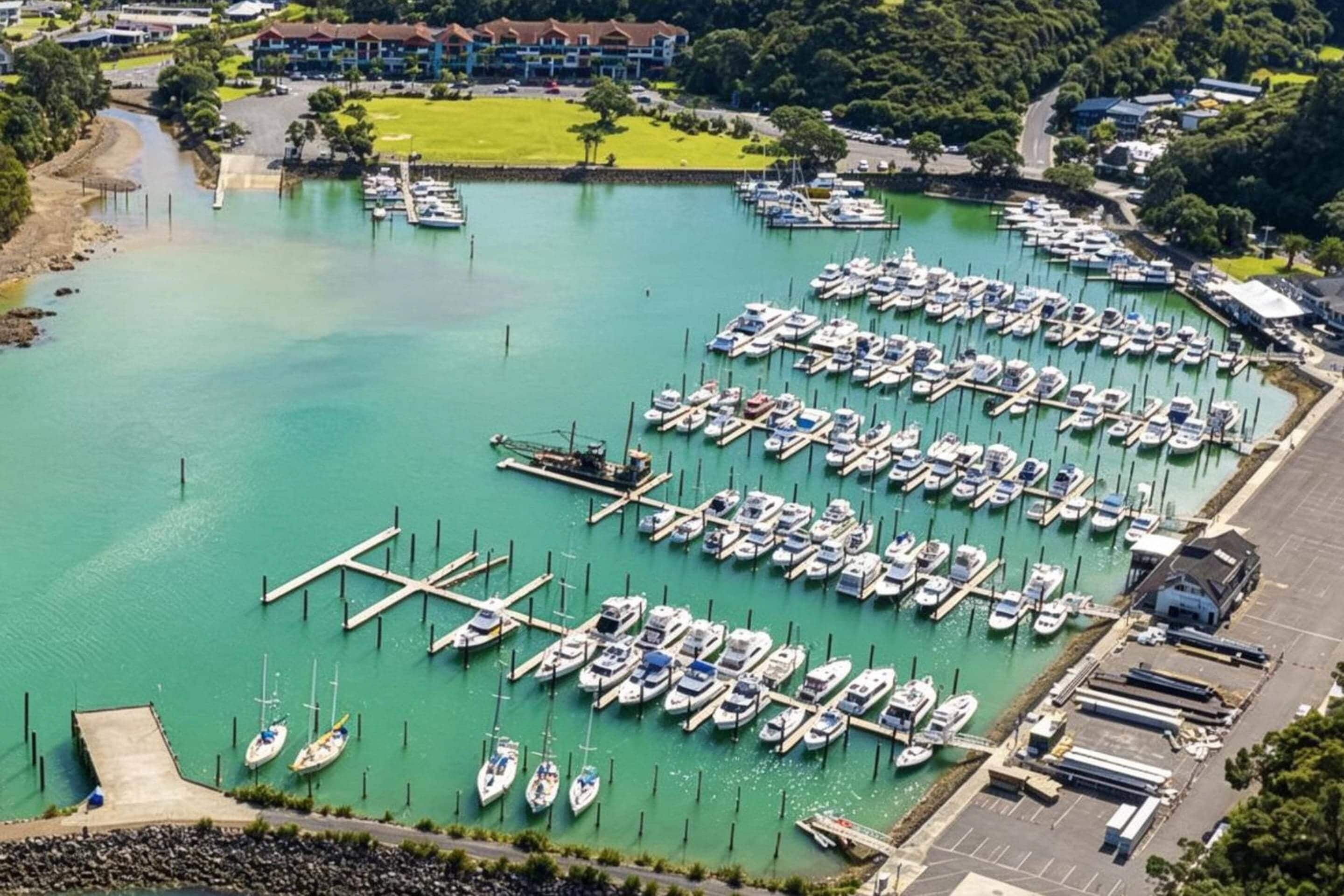 Een jachthaven met veel boten afgemeerd, een parkeerplaats en een gebouw op de achtergrond.