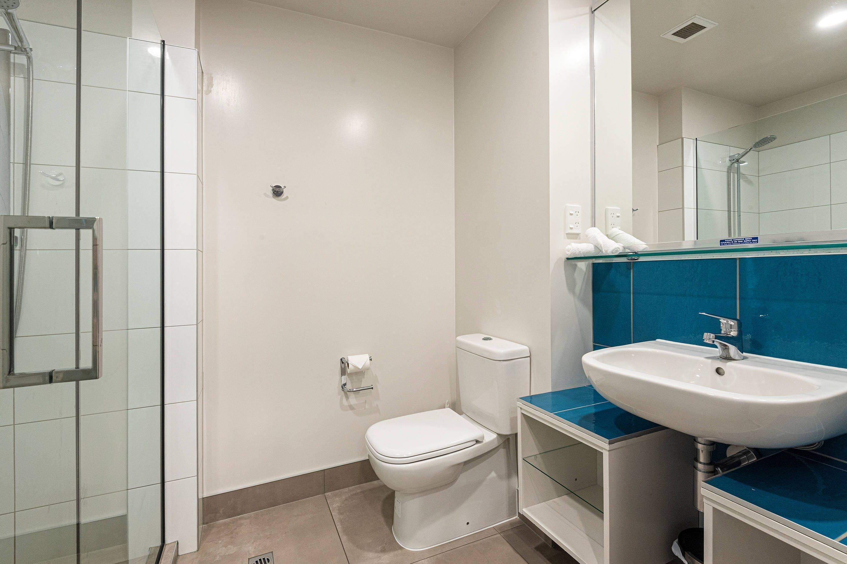 A bathroom with a glass shower enclosure, a white toilet, and a sink with a blue countertop.