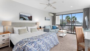 Ein Hotelzimmer mit Bett, Sofa, Schreibtisch, Stuhl, einem Balkon mit Blick und Deckenventilator.