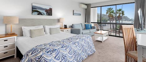 Et hotelværelse med en seng, en sofa, et skrivebord, en stol, en balkon med udsigt og en loftsvifte.