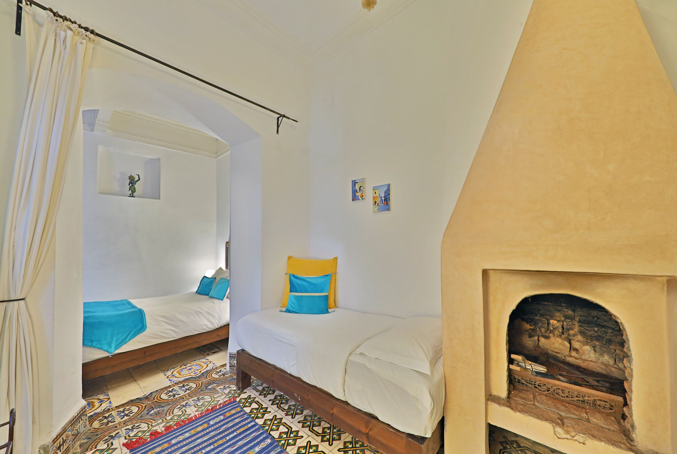 A room with two beds, a patterned floor, and a fireplace.