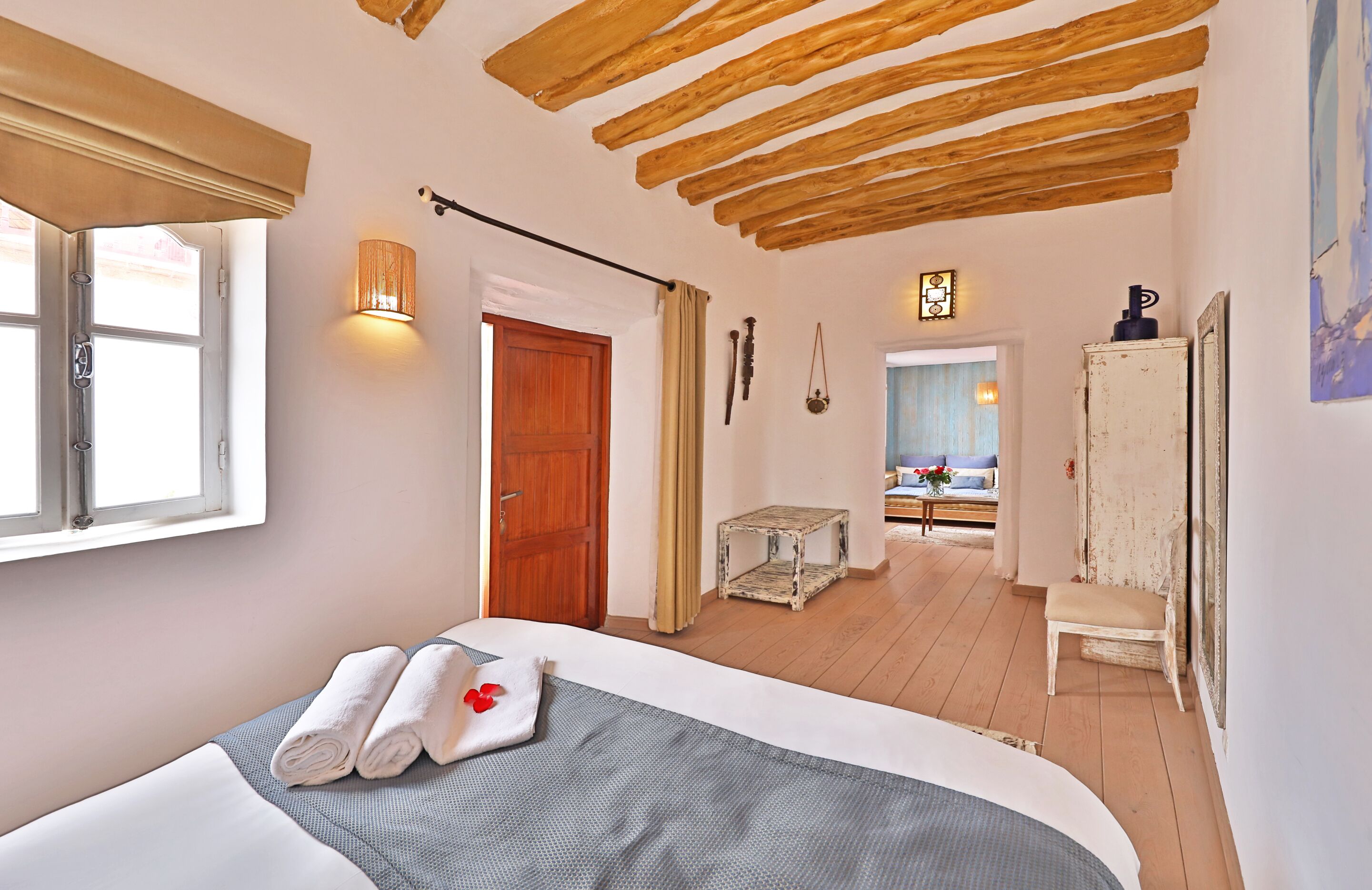 Une chambre à coucher avec un lit, un plafond en bois, une fenêtre, une porte et une vue sur une autre pièce.