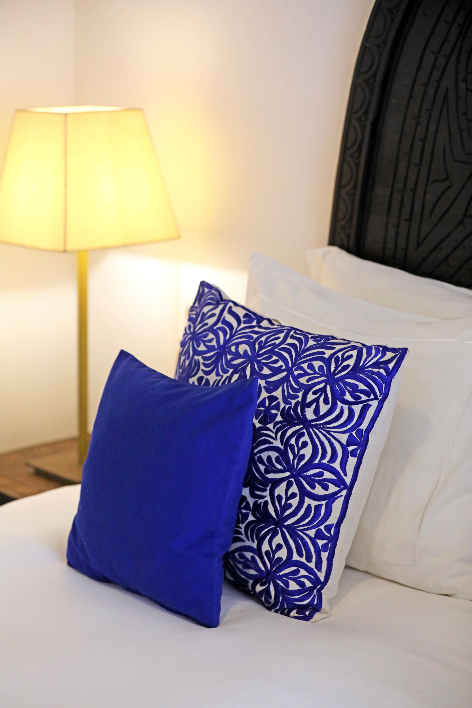 Ein Bett mit zwei Kissen, eines blau und eines weiß mit blauem Muster, und eine Lampe im Hintergrund.