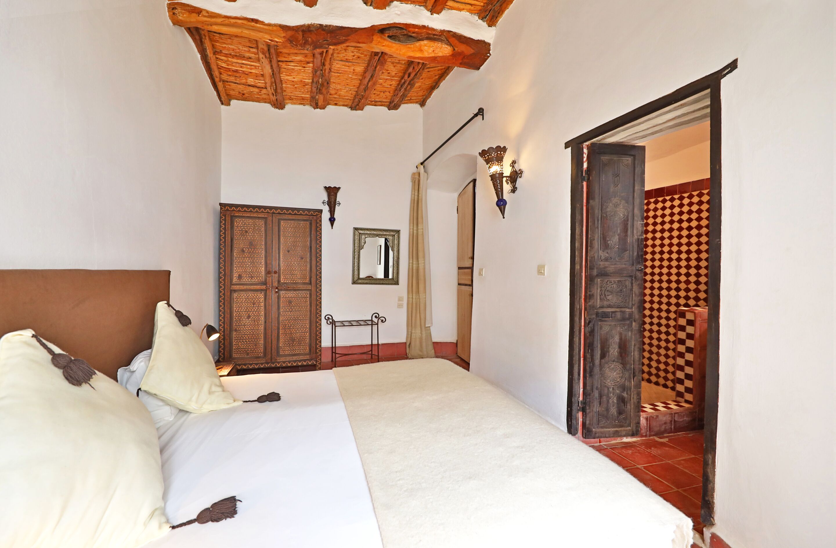 Une chambre à coucher avec un lit, un plafond en bois, une armoire, un miroir et un mur décoré de motifs.