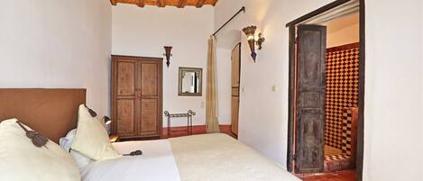 A bedroom with a bed, wooden ceiling, a wardrobe, a mirror, and a patterned wall.