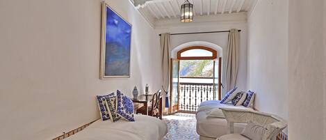 Un dormitorio con cama, una silla, un cuadro y vistas al exterior.