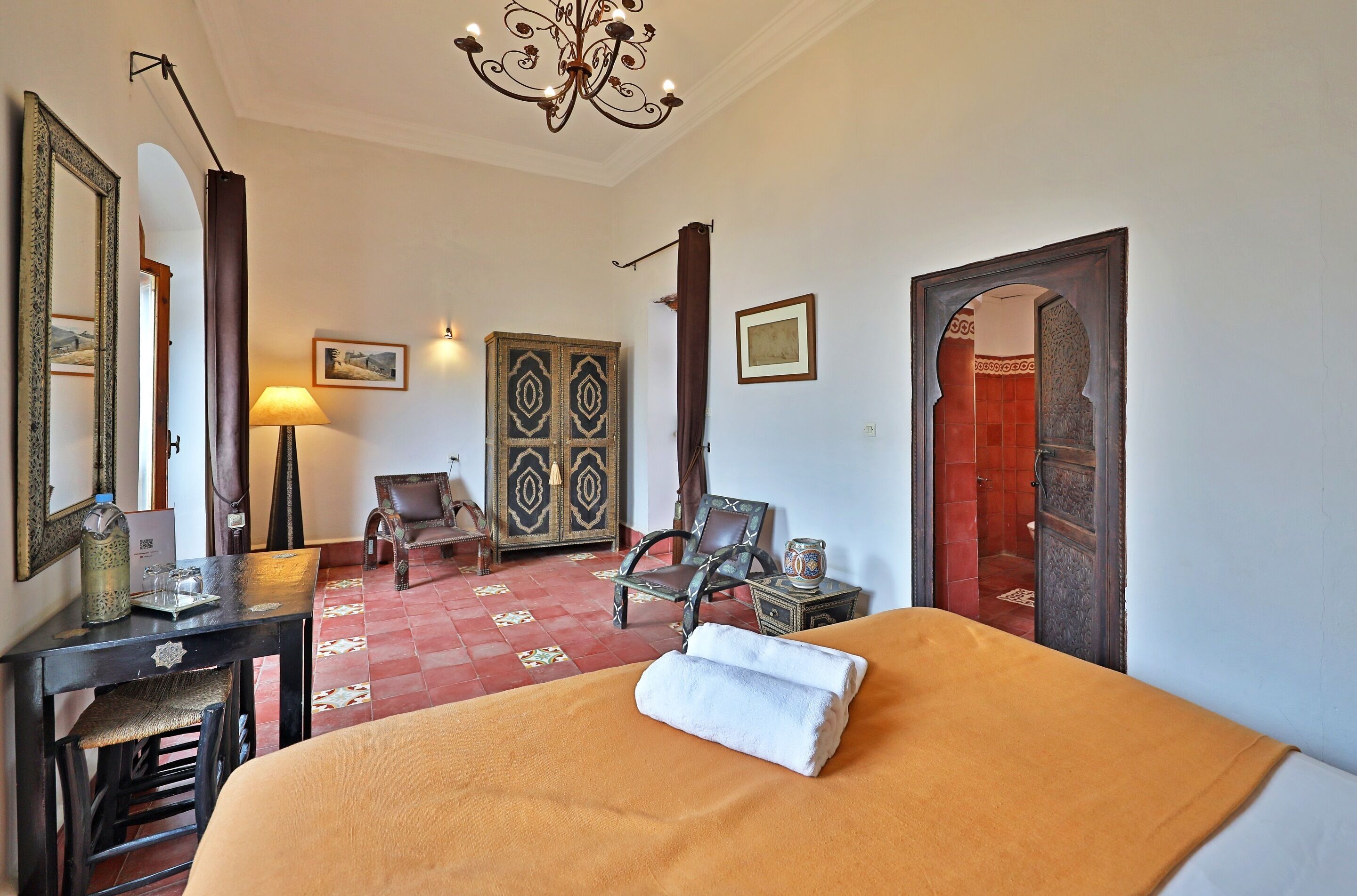 Una habitación de hotel con una cama, un escritorio, una silla, una lámpara y un espejo decorativo.