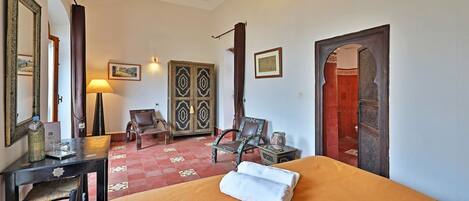 A hotel room with a bed, a desk, a chair, a lamp, and a decorative mirror.