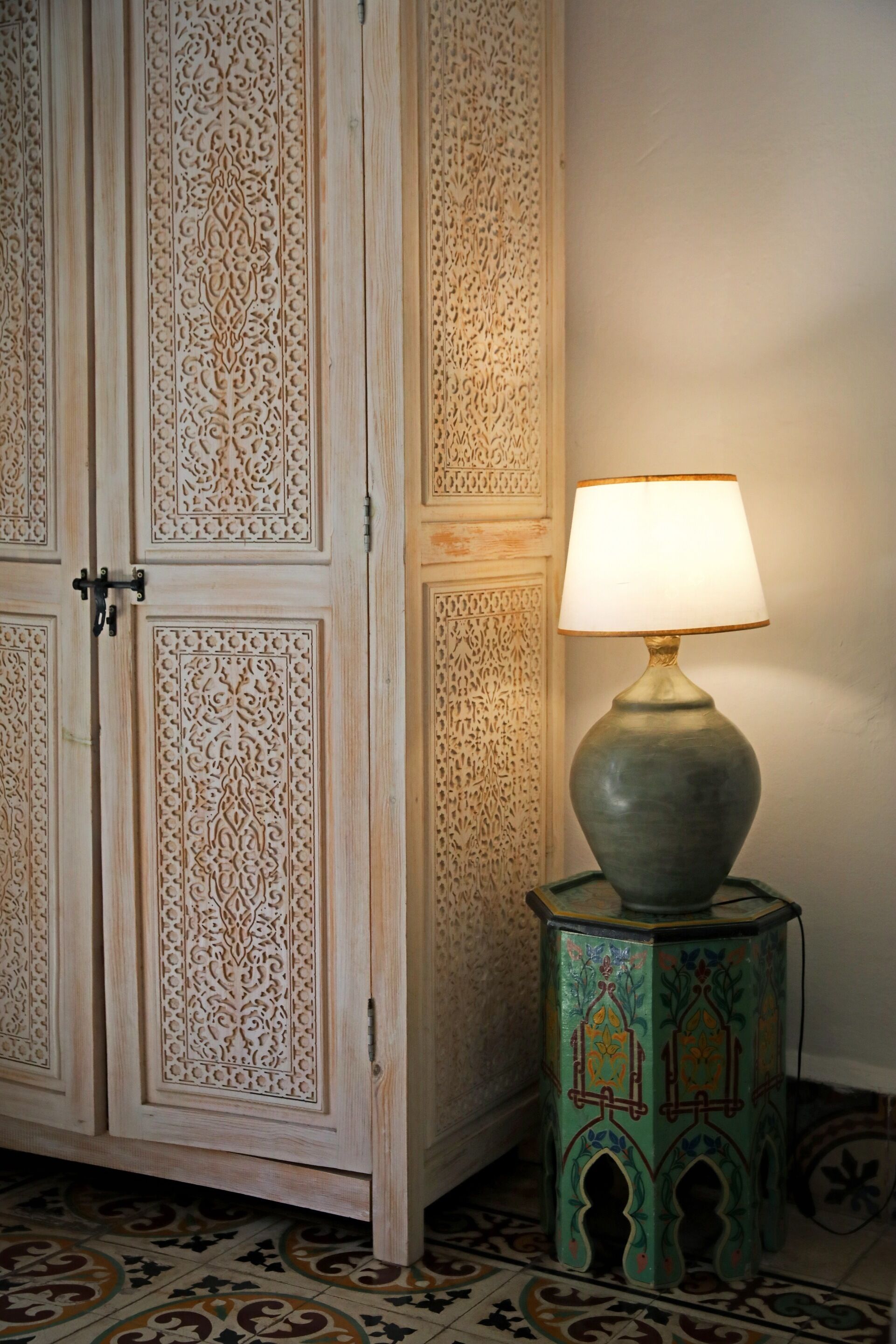 A room with a wooden cabinet featuring intricate carvings and a small, colorful side table with a lamp.