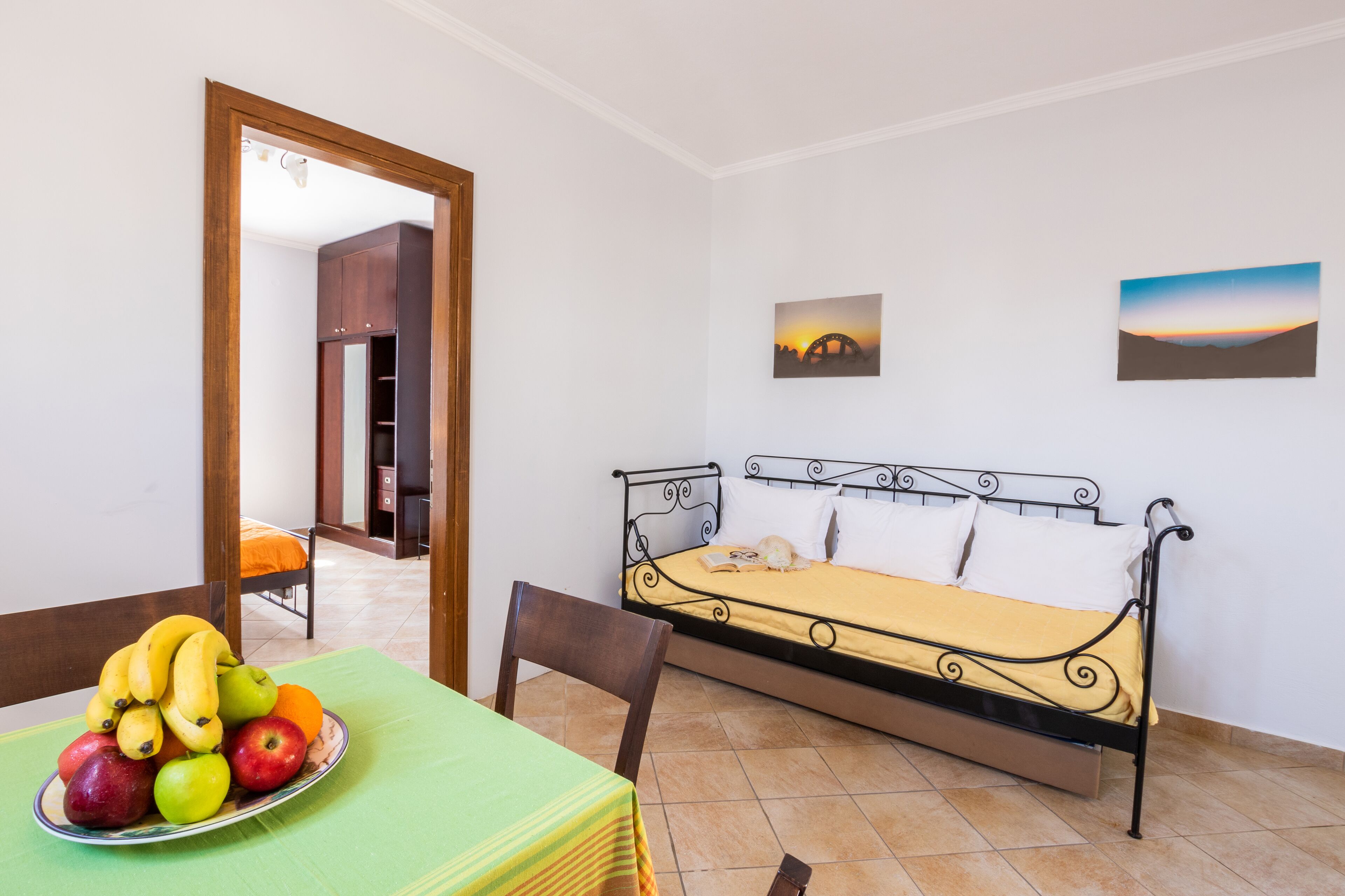 A room with a bed, a dining table with fruit, and a chair.