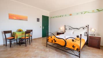 A bedroom with a bed, a nightstand, a bedside table, a chair, a table with a fruit bowl, and a green door.