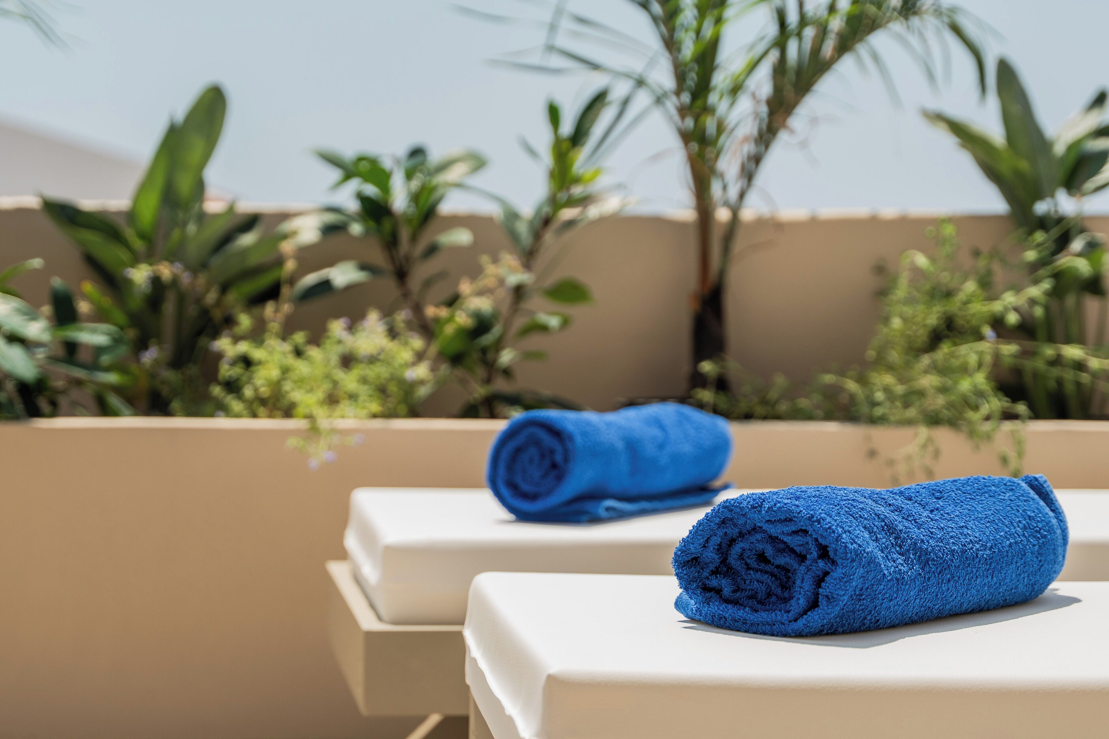 A sunlit outdoor seating area with two white lounge chairs and a blue towel on one.