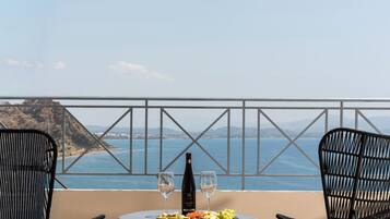 A table with a bottle of wine, two glasses, and a plate of food on a balcony overlooking a coastal view.