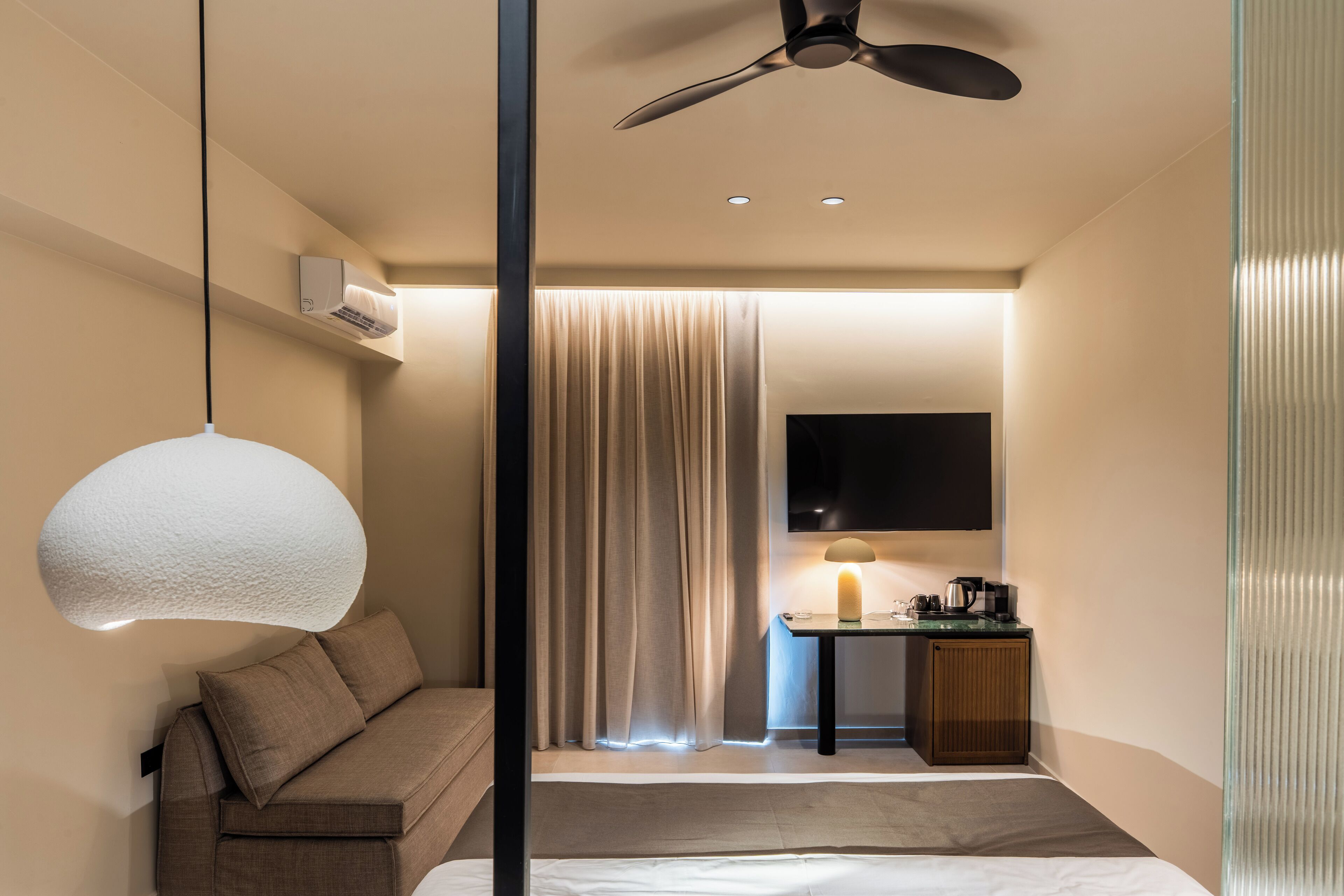 Una habitación de hotel moderna con una cama, un sofá, un escritorio con lámpara y un ventilador de techo.