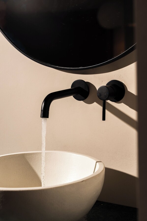 Un lavabo en céramique blanche, placé sous un robinet noir, et dans lequel l’eau coule.