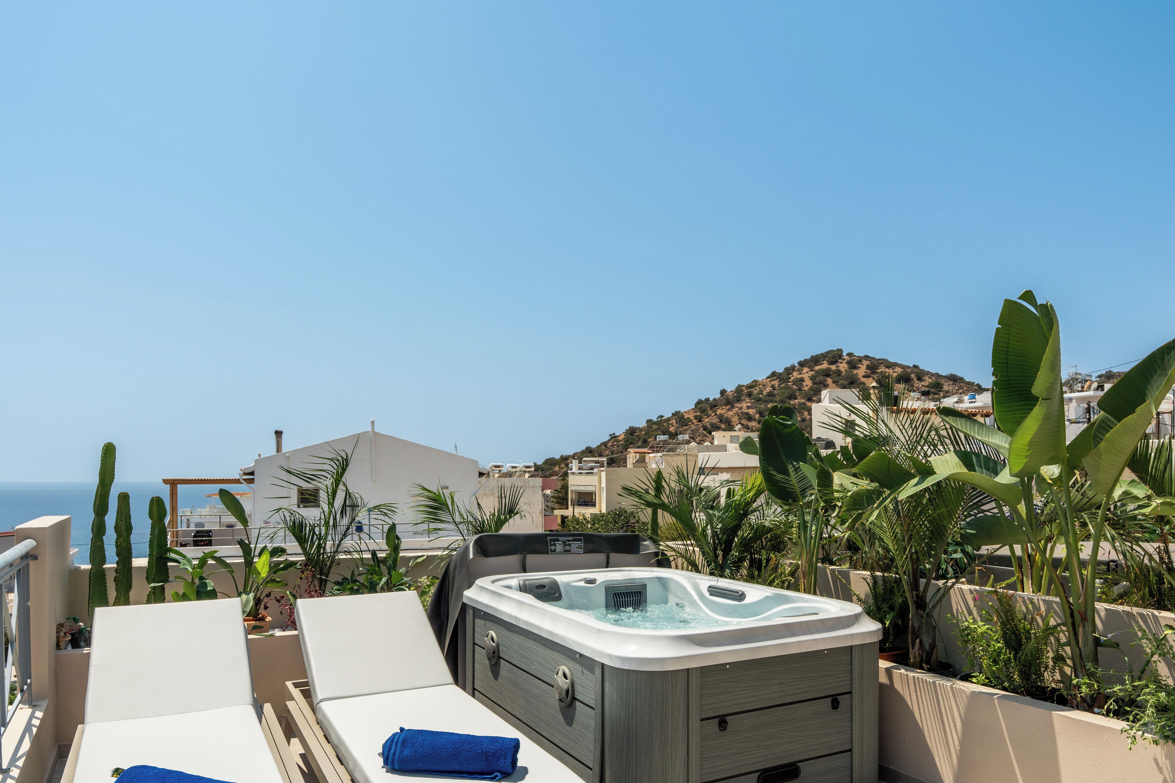 A rooftop terrace with a hot tub, lounge chairs, and a view of the sea and hills.