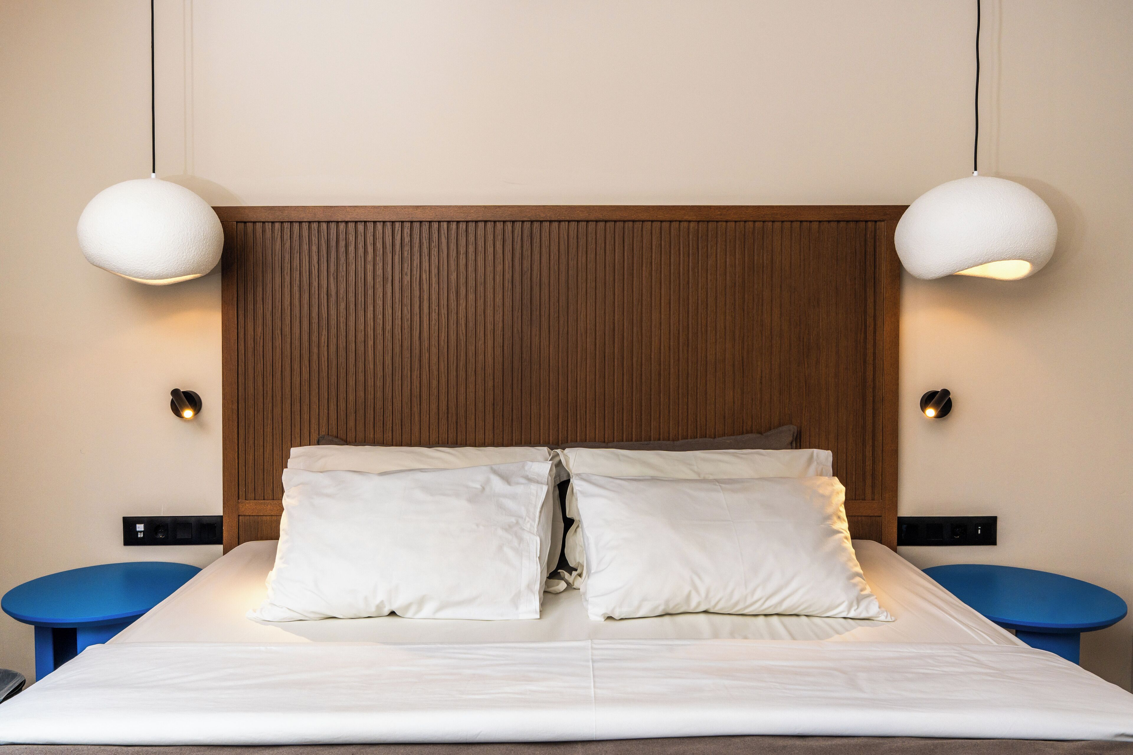Una cama bien hecha con sábanas blancas, cabecera de madera y dos lámparas colgantes.