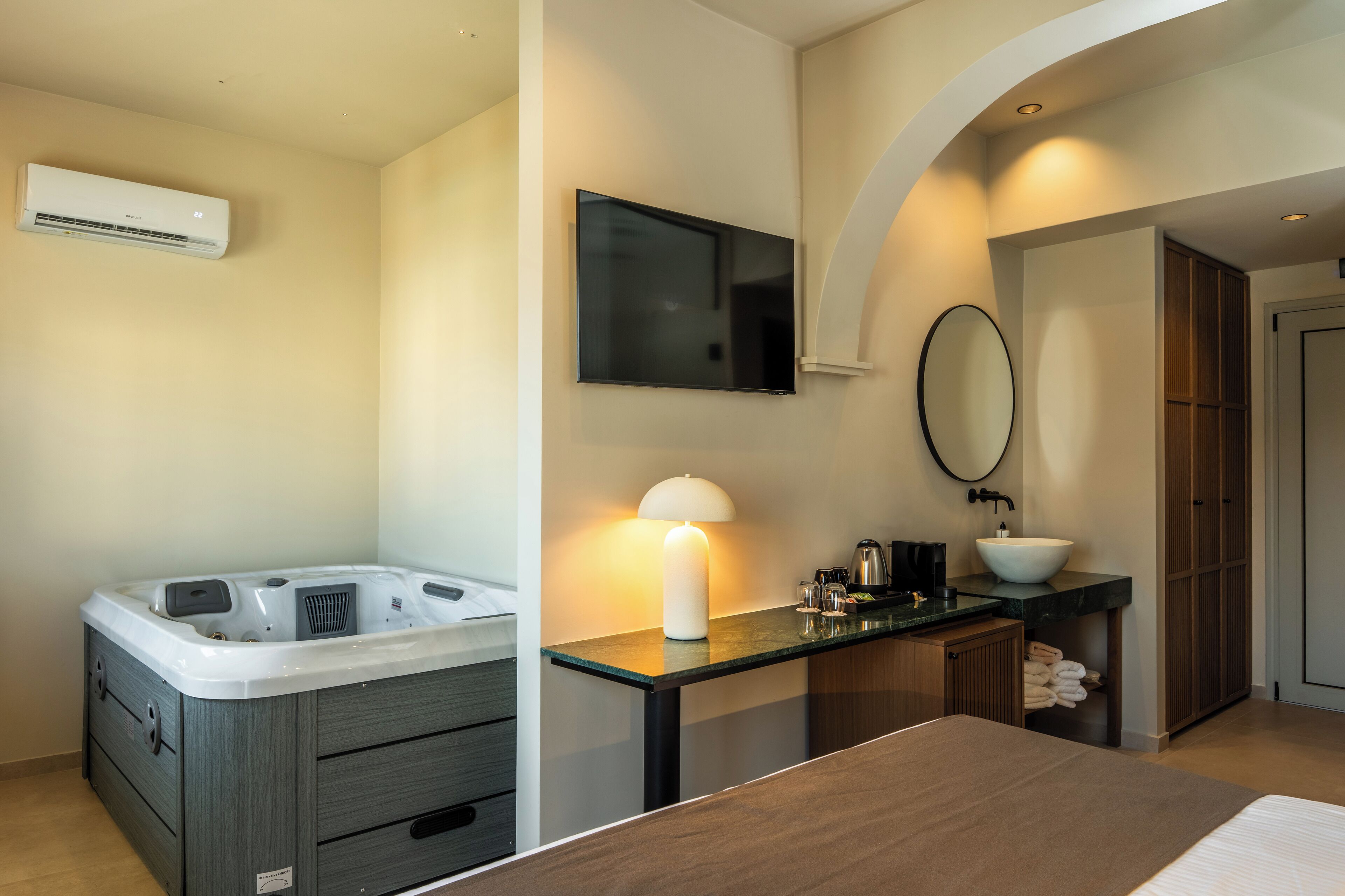 A modern bathroom with a bathtub, a vanity with a sink, a mirror, and a television mounted on the wall.