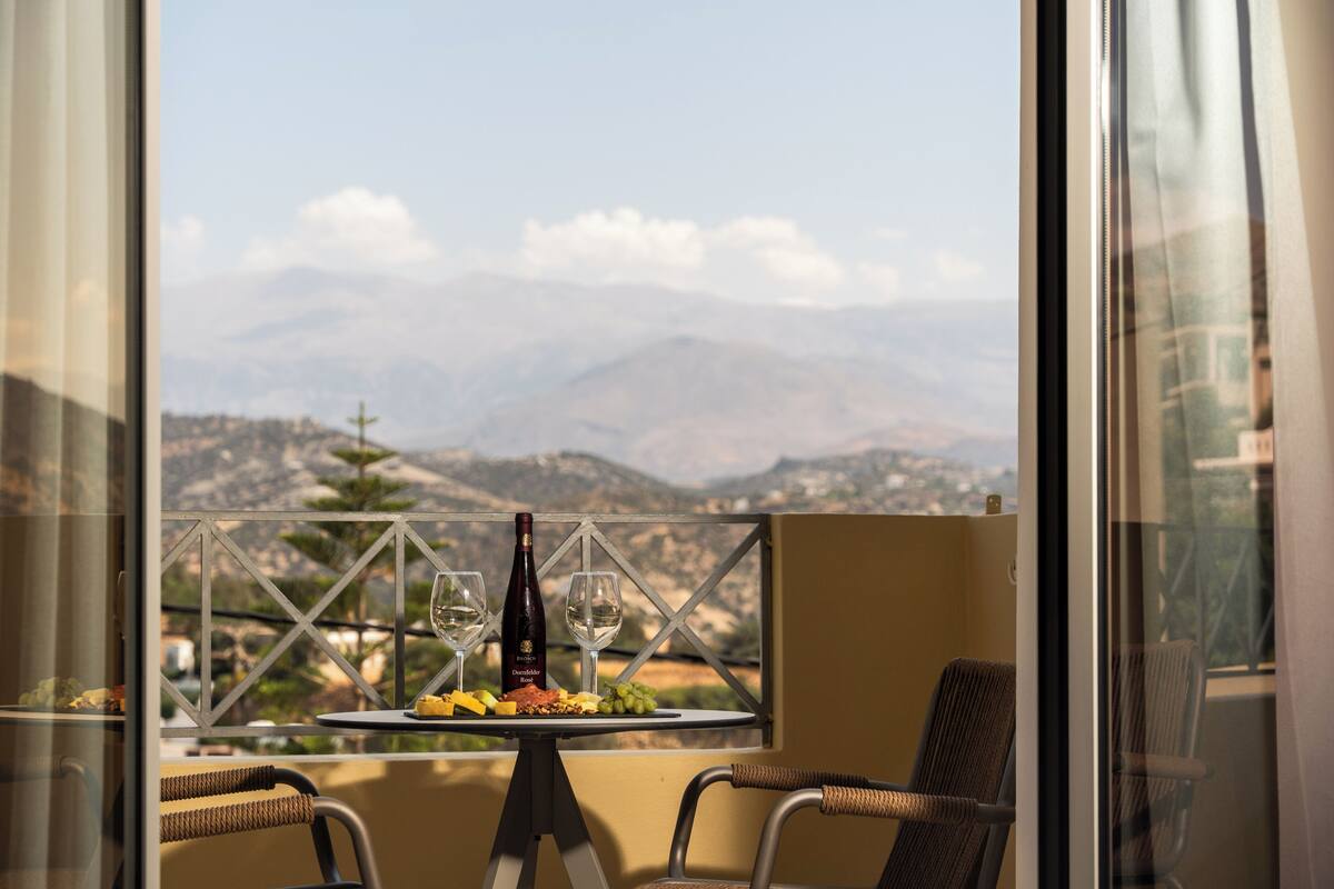 A balcony with a table set for two, featuring a bottle of wine, two glasses, and a plate of food.