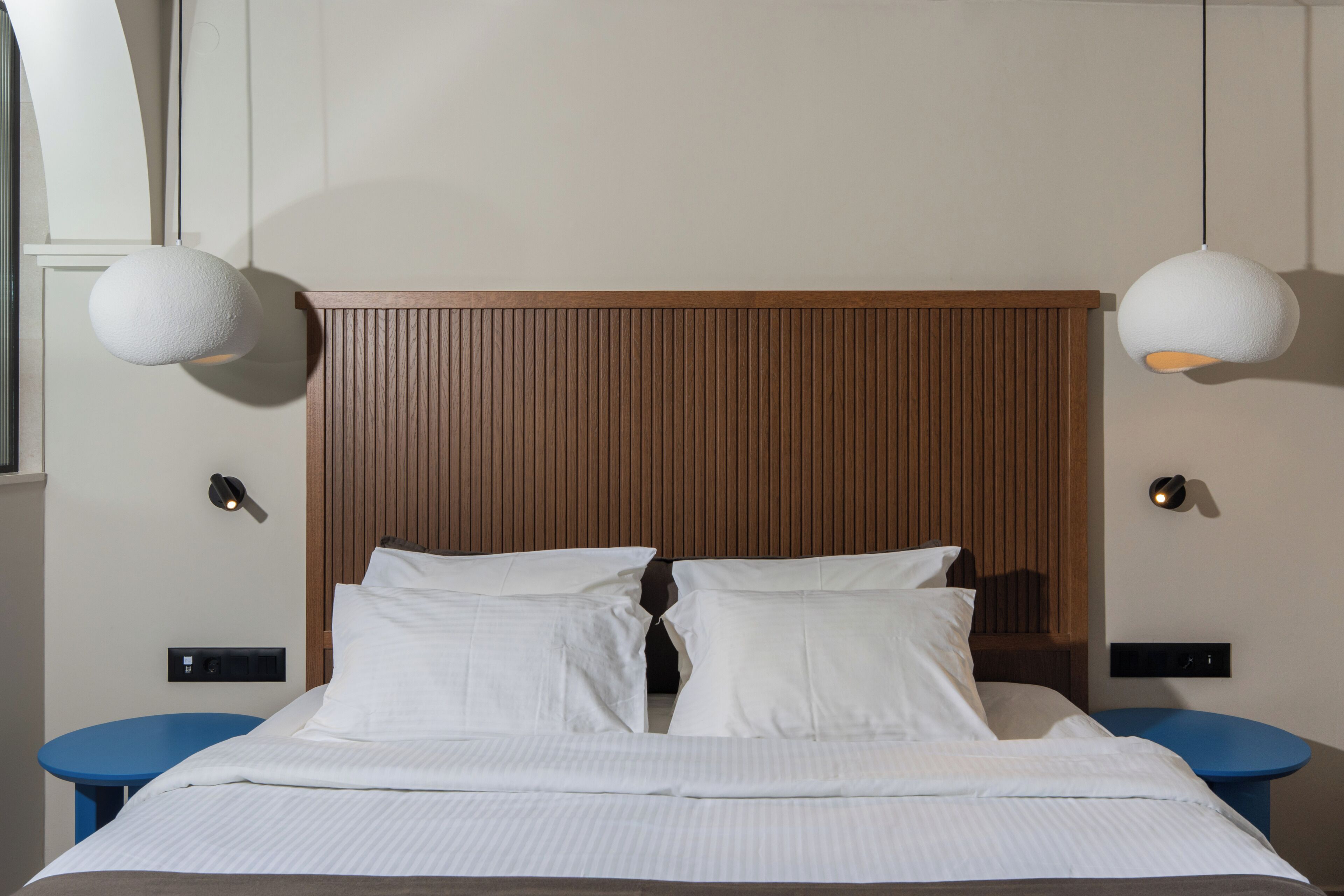 Una cama bien hecha con sábanas blancas, dos mesitas de noche y un cabecero de madera.
