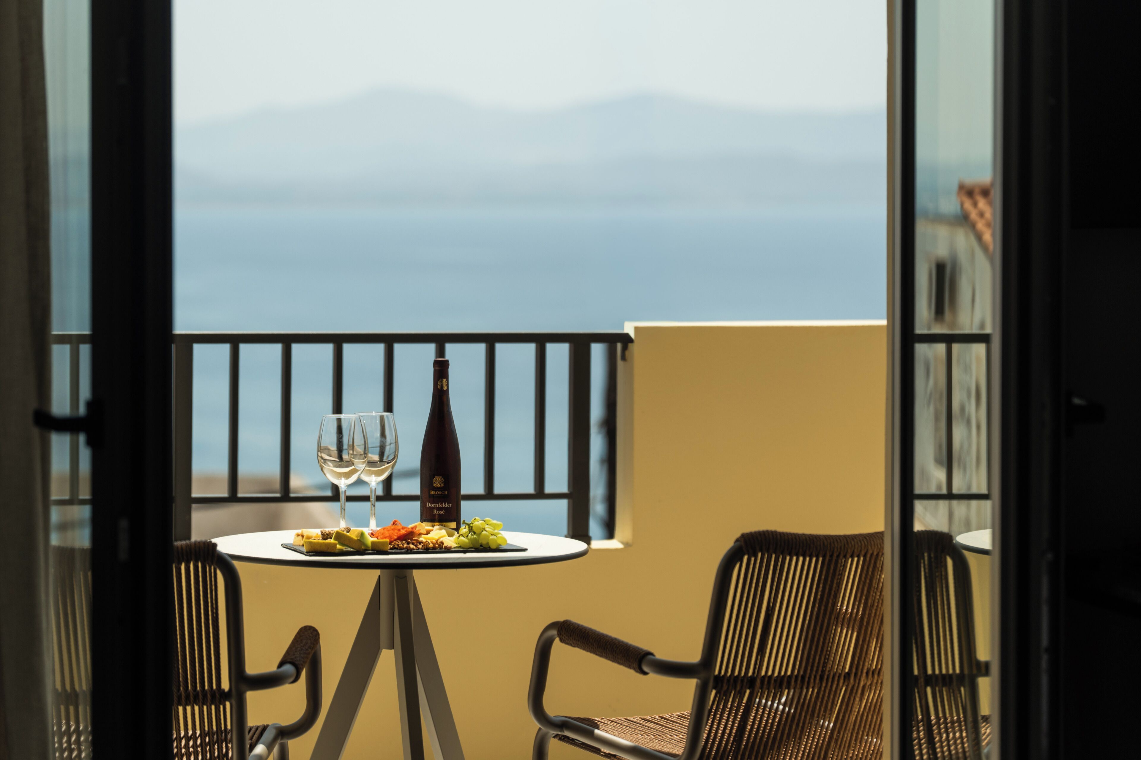 A balcony with a table set for two, a bottle of wine, and a view of the sea.