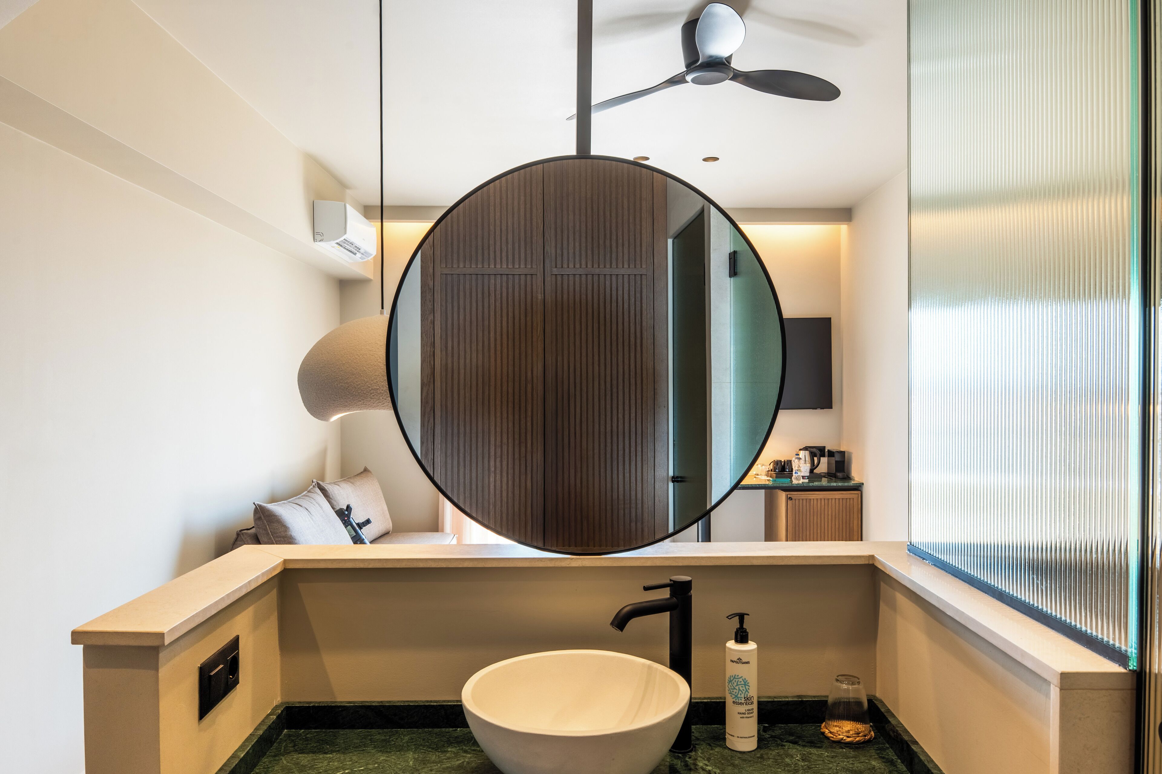 A modern bathroom with a round mirror, a vessel sink, and a ceiling fan.