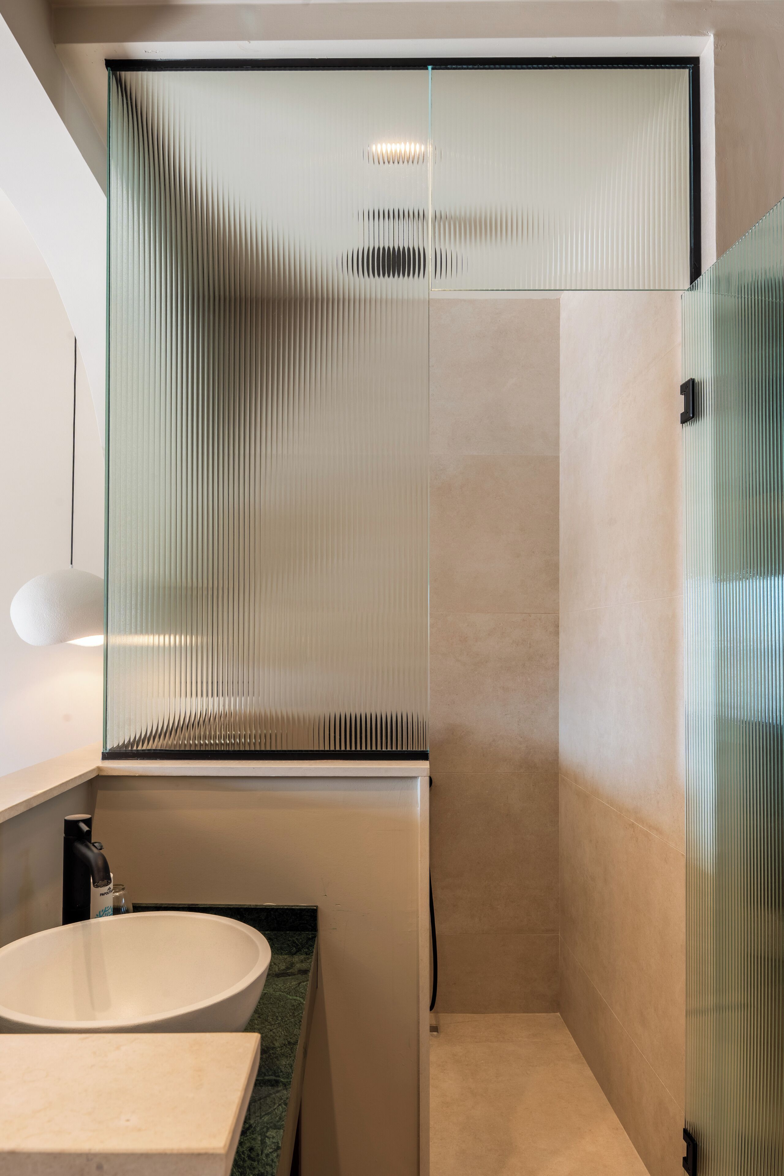 Ein modernes Badezimmer mit einer Duschkabine aus Glas, einem weißen Waschbecken und einer Marmorarbeitsplatte.