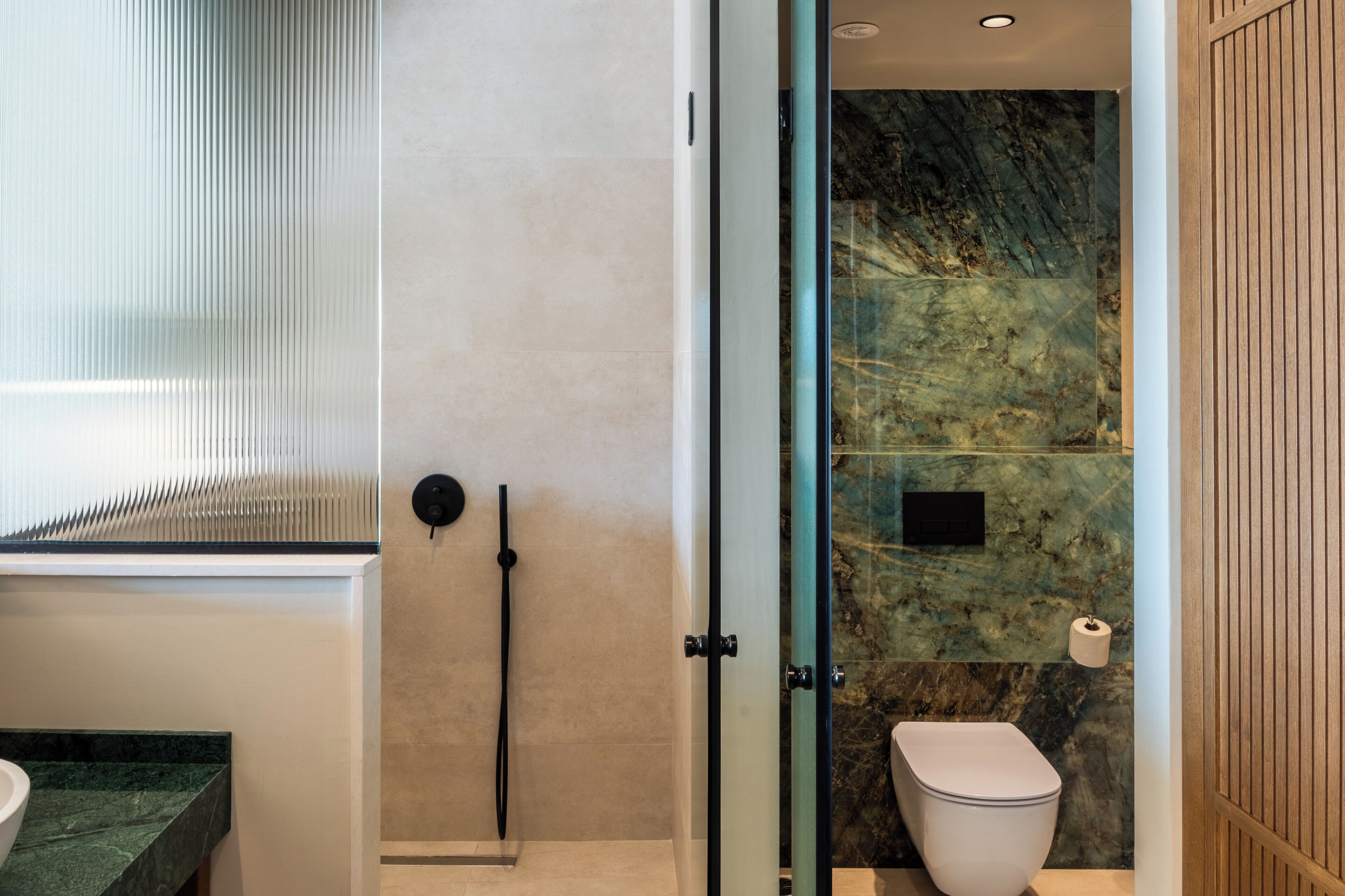 A modern bathroom with a glass shower enclosure, a marble wall, and a wooden panel.