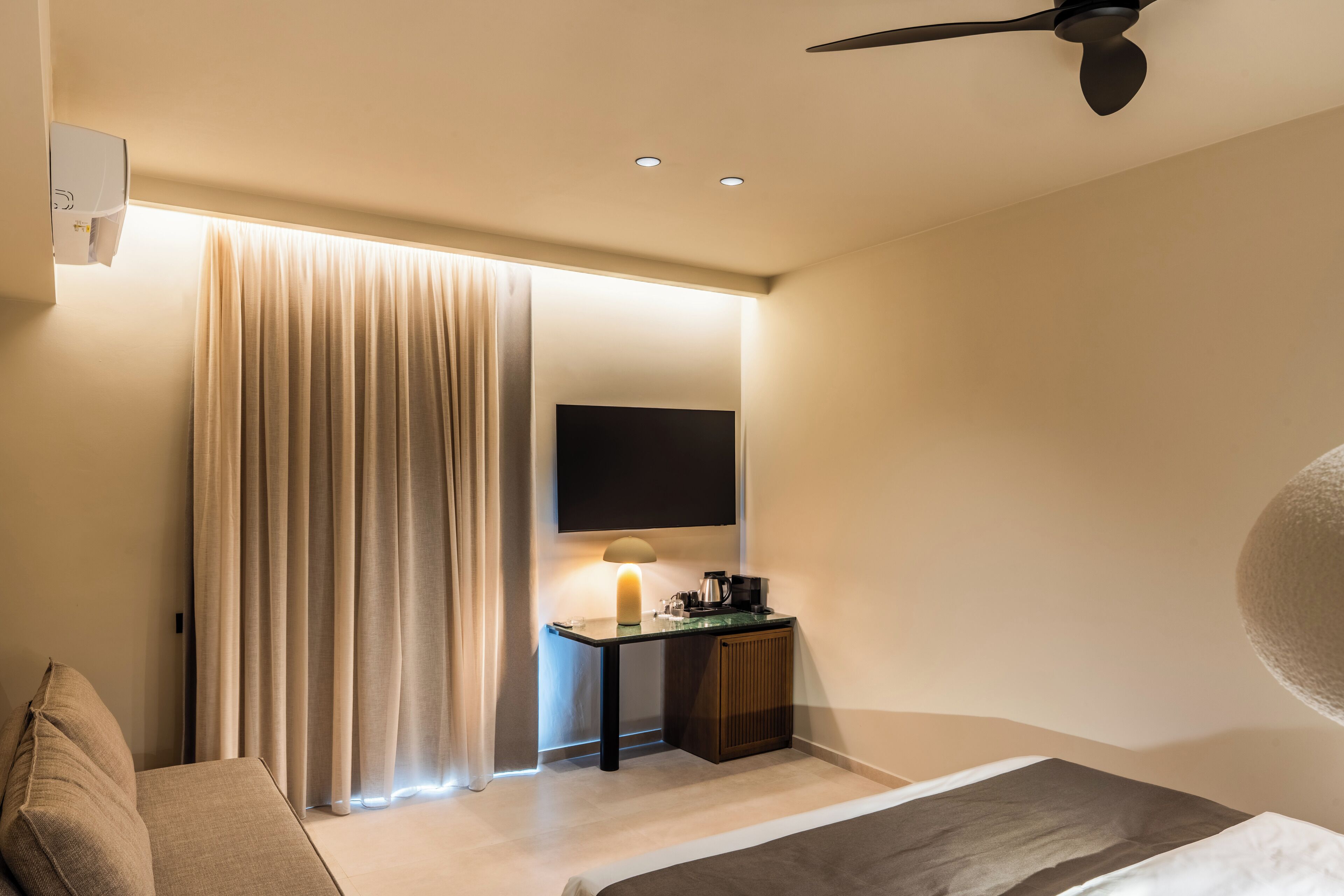 A modern hotel room with a bed, a desk with a lamp, a flat-screen TV, and a ceiling fan.
