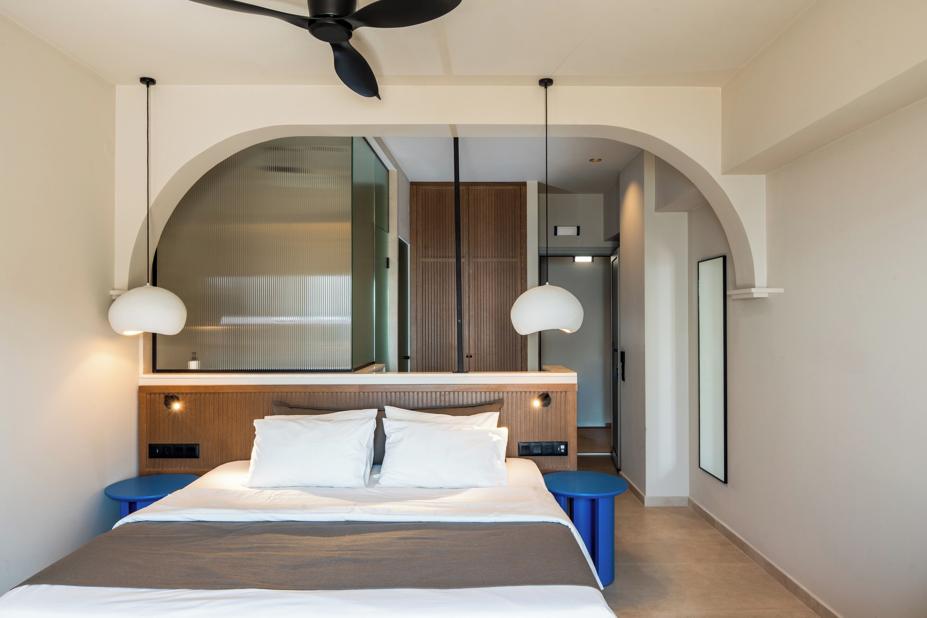 A modern hotel room with a large bed, two bedside tables, a ceiling fan, and a large mirror above the bed.