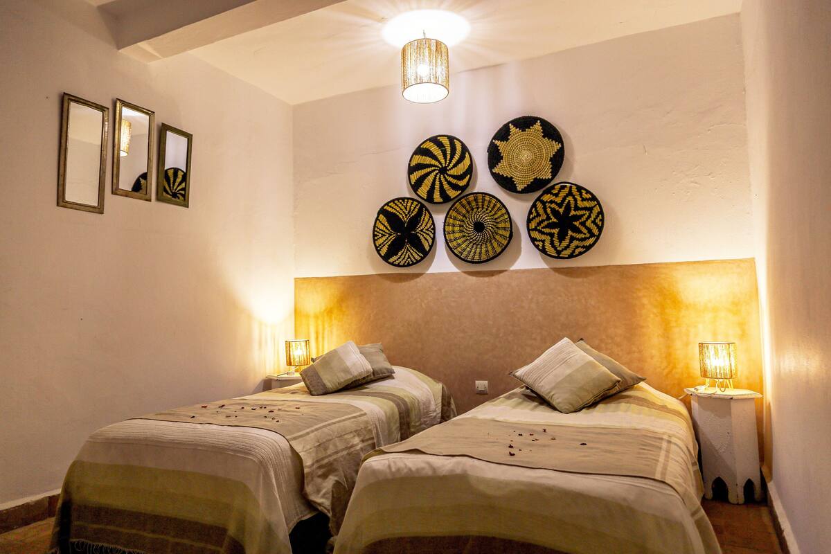 A hotel room with two beds, a chandelier, wall-mounted mirrors, and decorative plates.