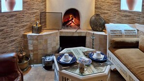 A cozy room with a stone fireplace, two wall-mounted lights, and a cushioned seating area. - Dar Nafoura Mogador (Essaouira)