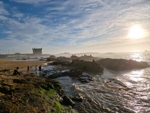 Un paysage côtier avec un terrain rocheux, une structure ressemblant à un château et l’océan.