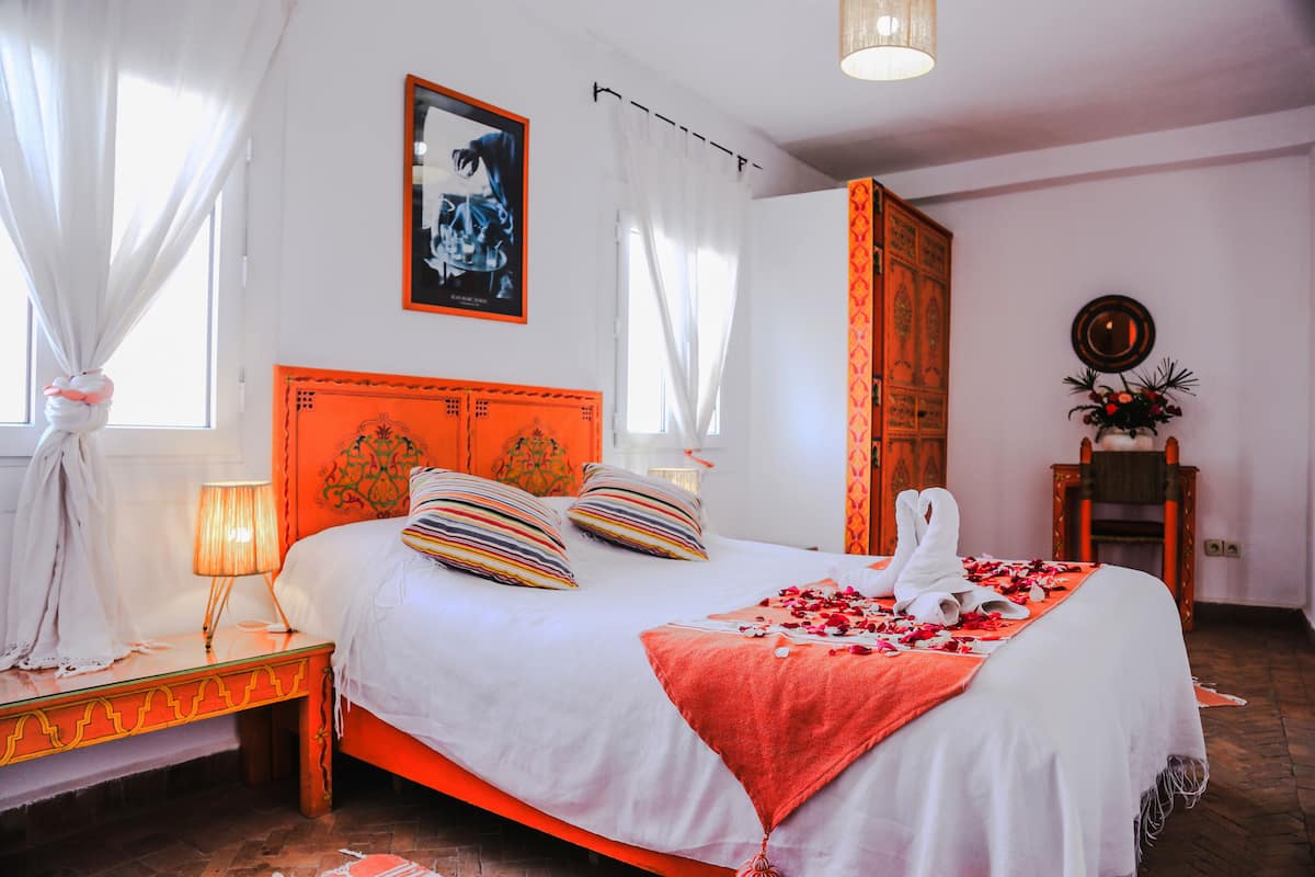 A hotel room with a bed, a nightstand, a lamp, a mirror, and a window with curtains.
