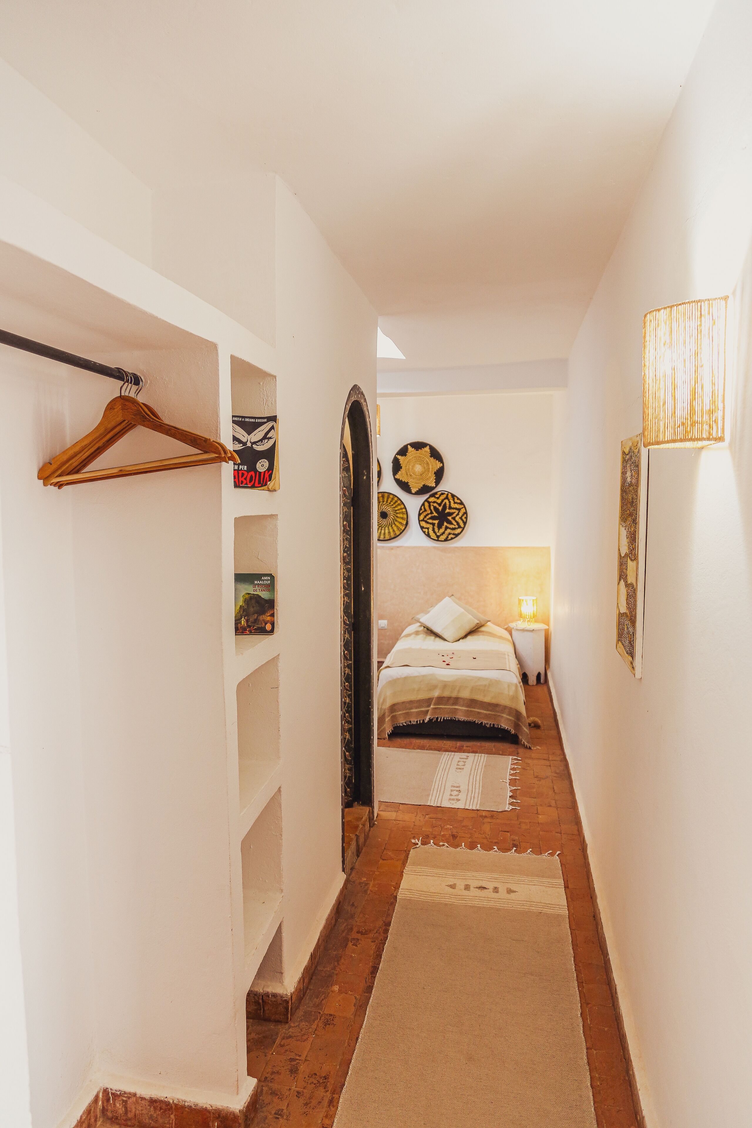 Un pasillo estrecho con una cama al final, un perchero de madera y adornos en la pared.