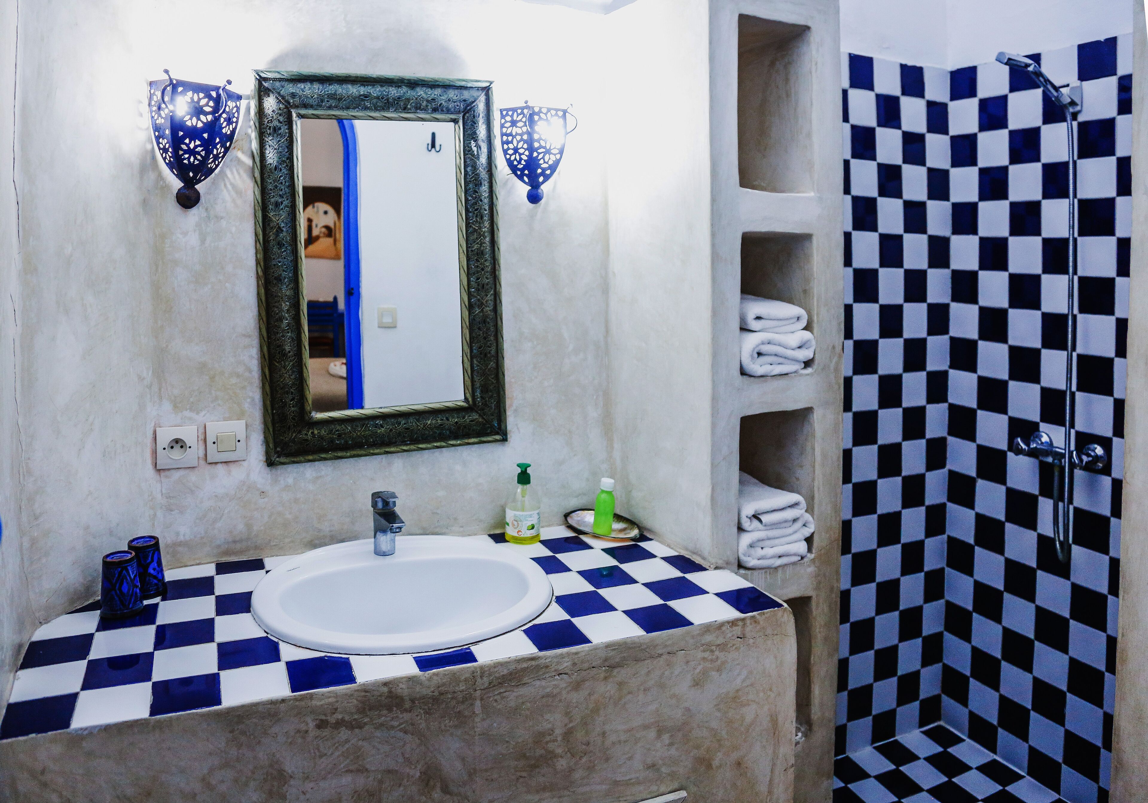 Un baño con piso de baldosas a cuadros, un lavamanos blanco, un espejo con marco decorativo y una ducha con azulejos a cuadros.