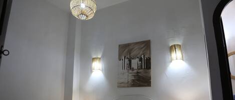 Una cama bien hecha con sábanas blancas, dos lámparas de noche, un cuadro en la pared y un aplique decorativo encima.