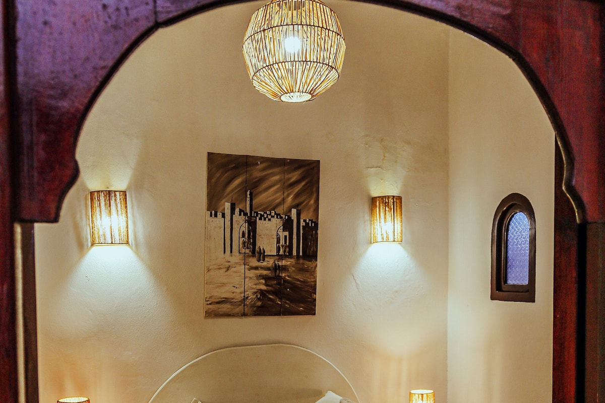 A bedroom with a bed, two bedside lamps, a wall-mounted light fixture, and a small window.