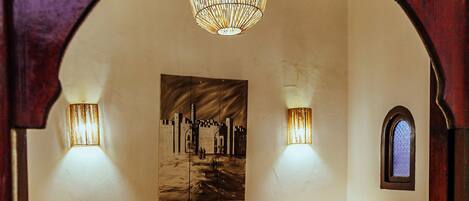 A bedroom with a bed, two bedside lamps, a wall-mounted light fixture, and a small window.