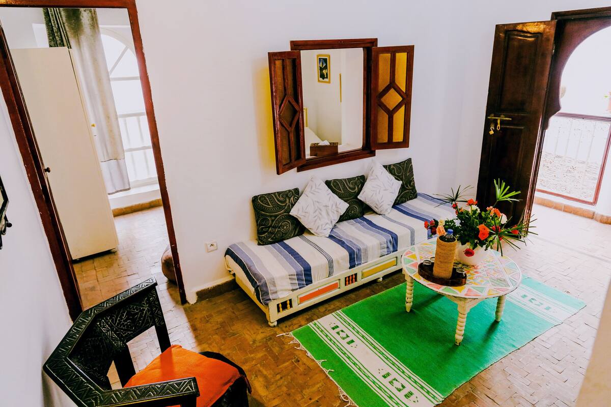 A room with a bed, a table with a vase of flowers, a mirror, and a door.