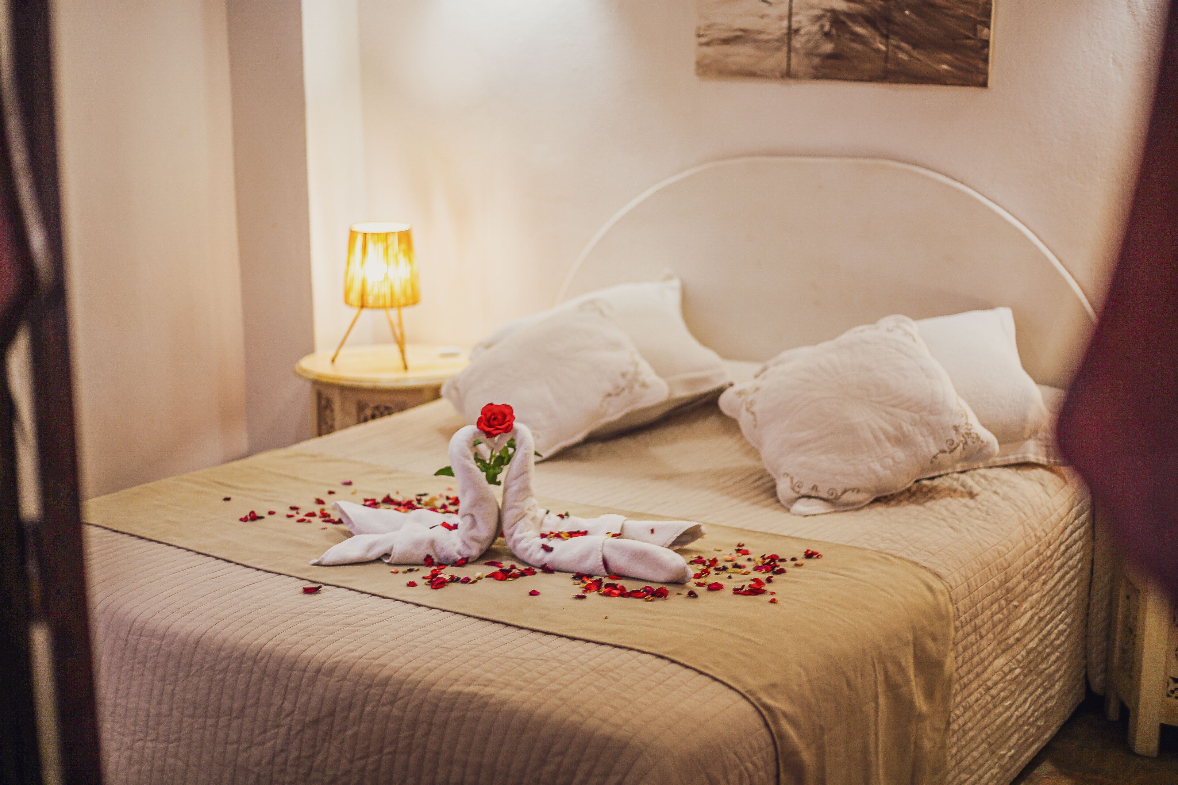 Ein ordentlich bezogenes Bett mit einer beige farbenen Tagesdecke, weißen Kissen und einer dekorativen Schwanenform aus Handtüchern mit einer Rose.