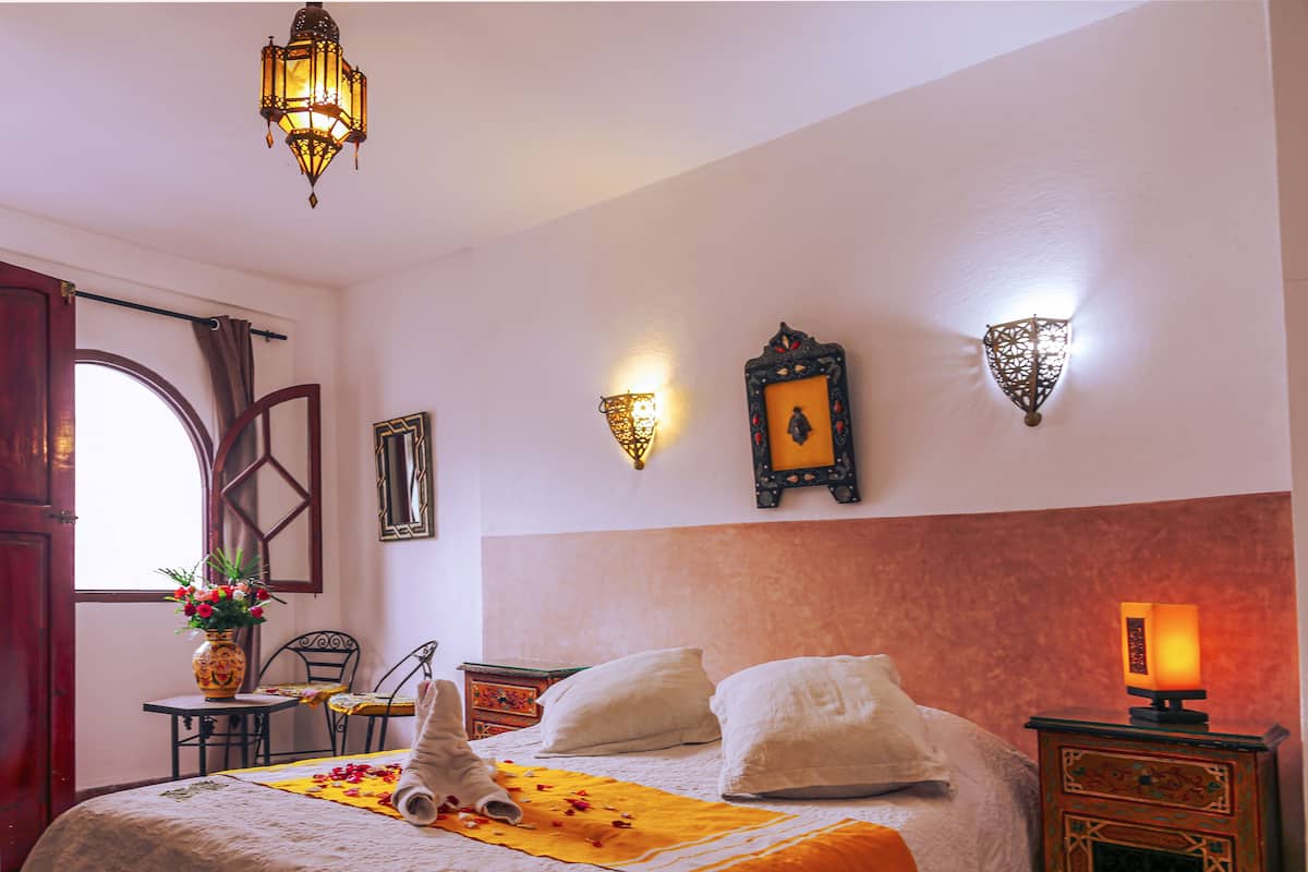 A hotel room with a bed, a nightstand, a table with a vase of flowers, and wall-mounted lights.