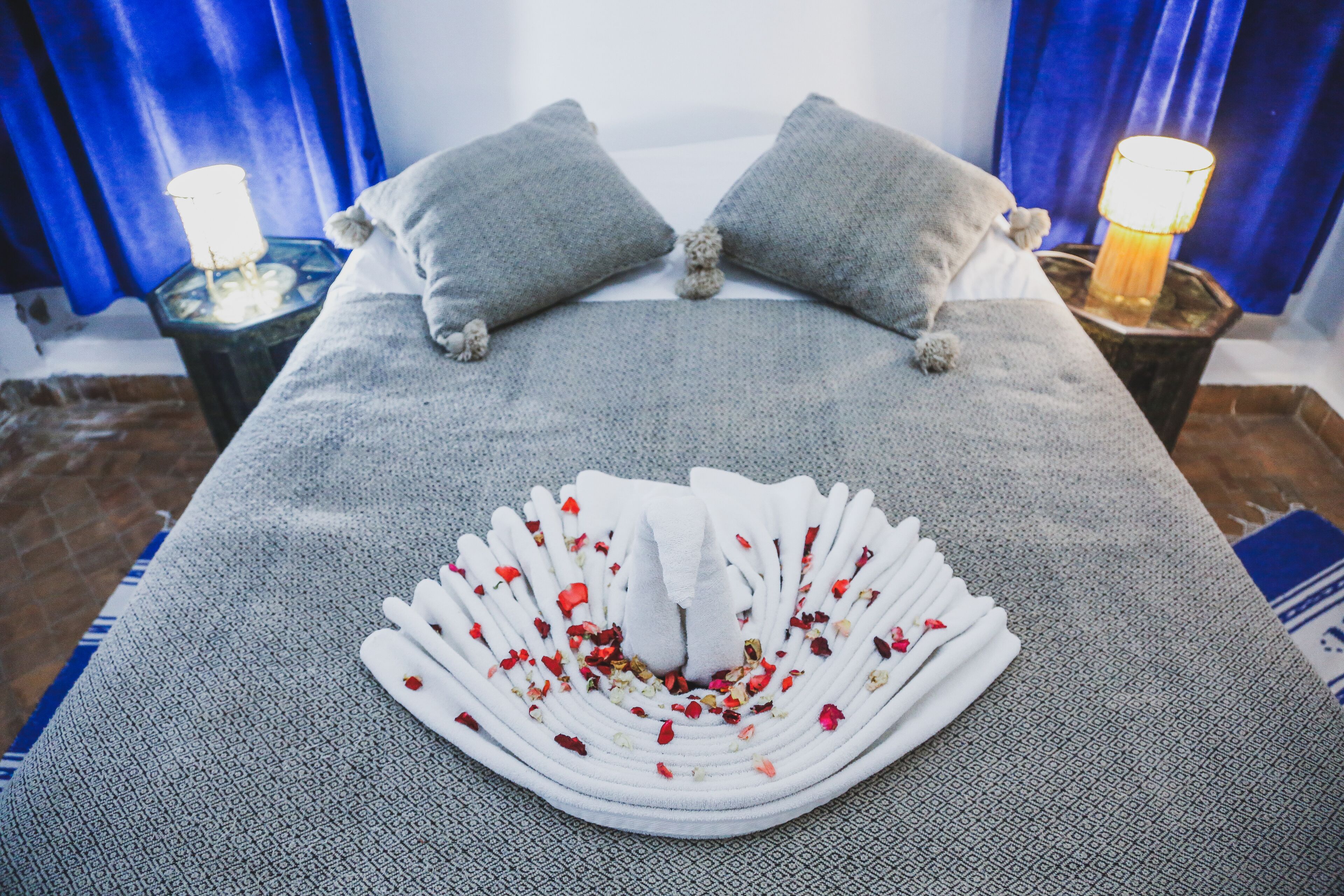 Una cama bien hecha con un adorno decorativo, almohadas y una mesita de noche con lámpara.