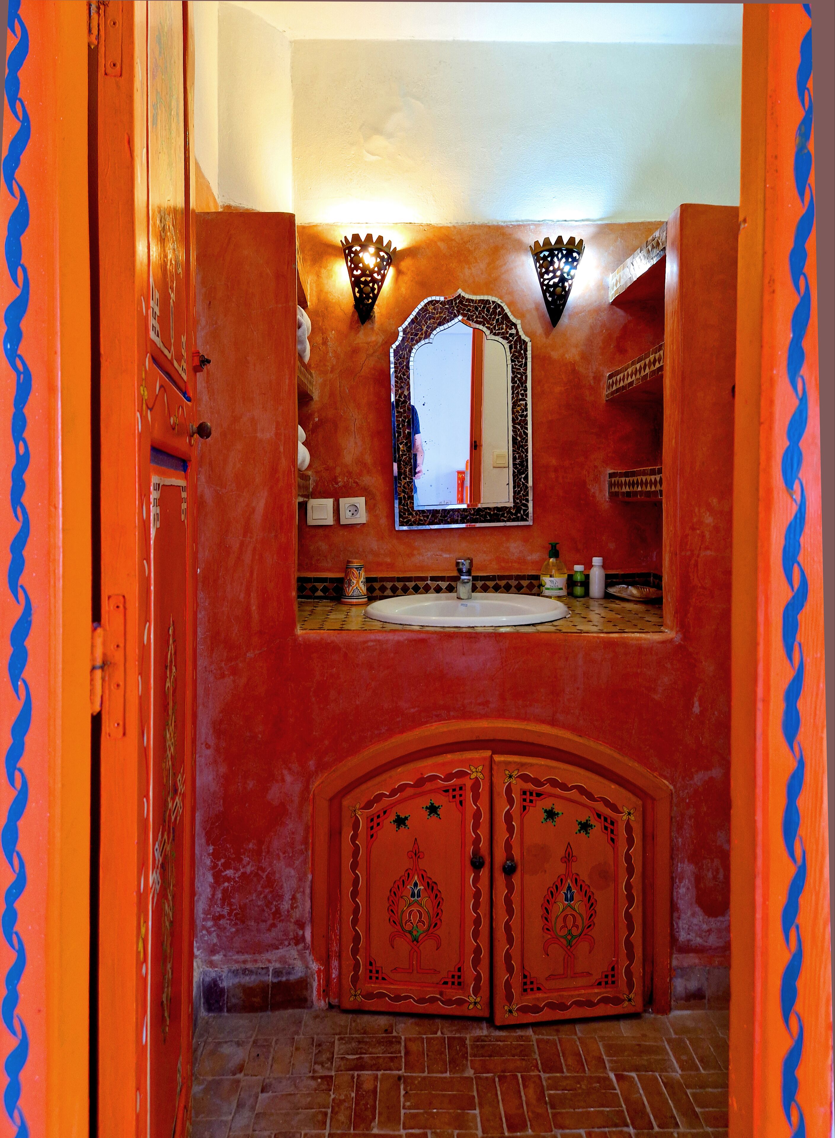 A bathroom with a red tiled wall, a white sink, and a mirror above it.