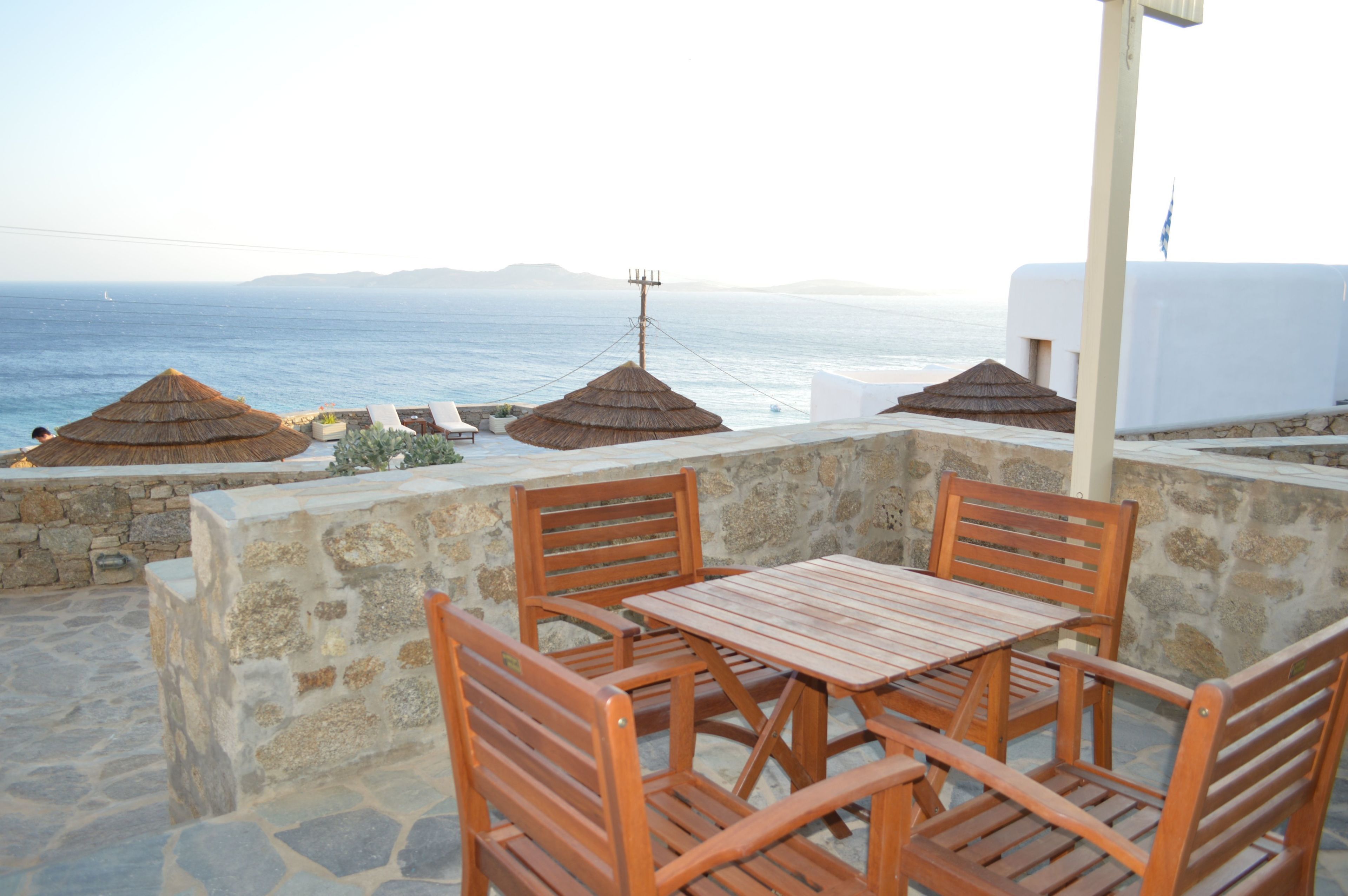 A terrace with wooden furniture and thatched umbrellas overlooking the sea.