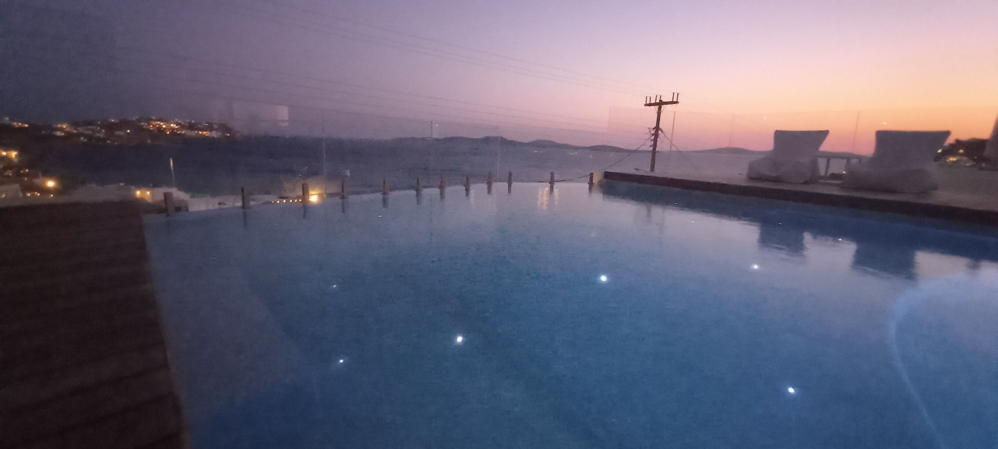 A swimming pool with lounge chairs and a view of a distant cityscape at dusk.