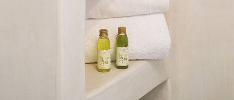 Un baño con toallas blancas y botellas de aceite de oliva en estantes.