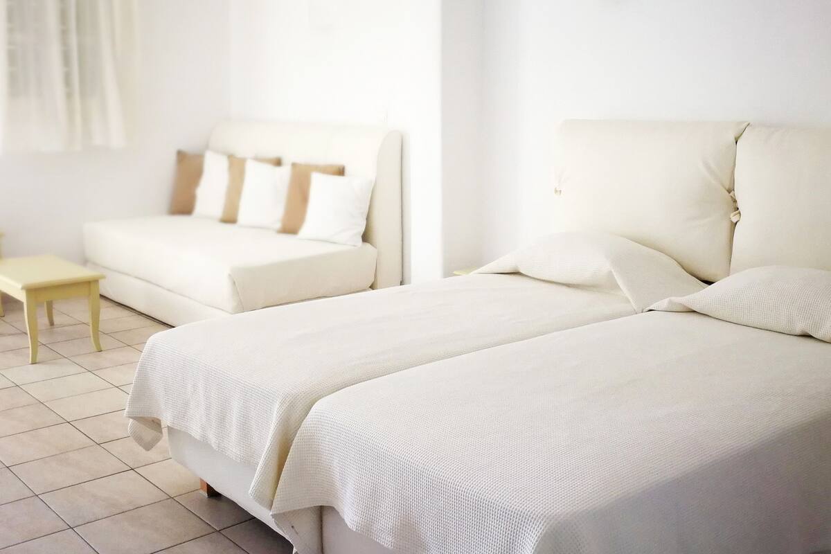 A hotel room with two beds, a small table, and a sofa.