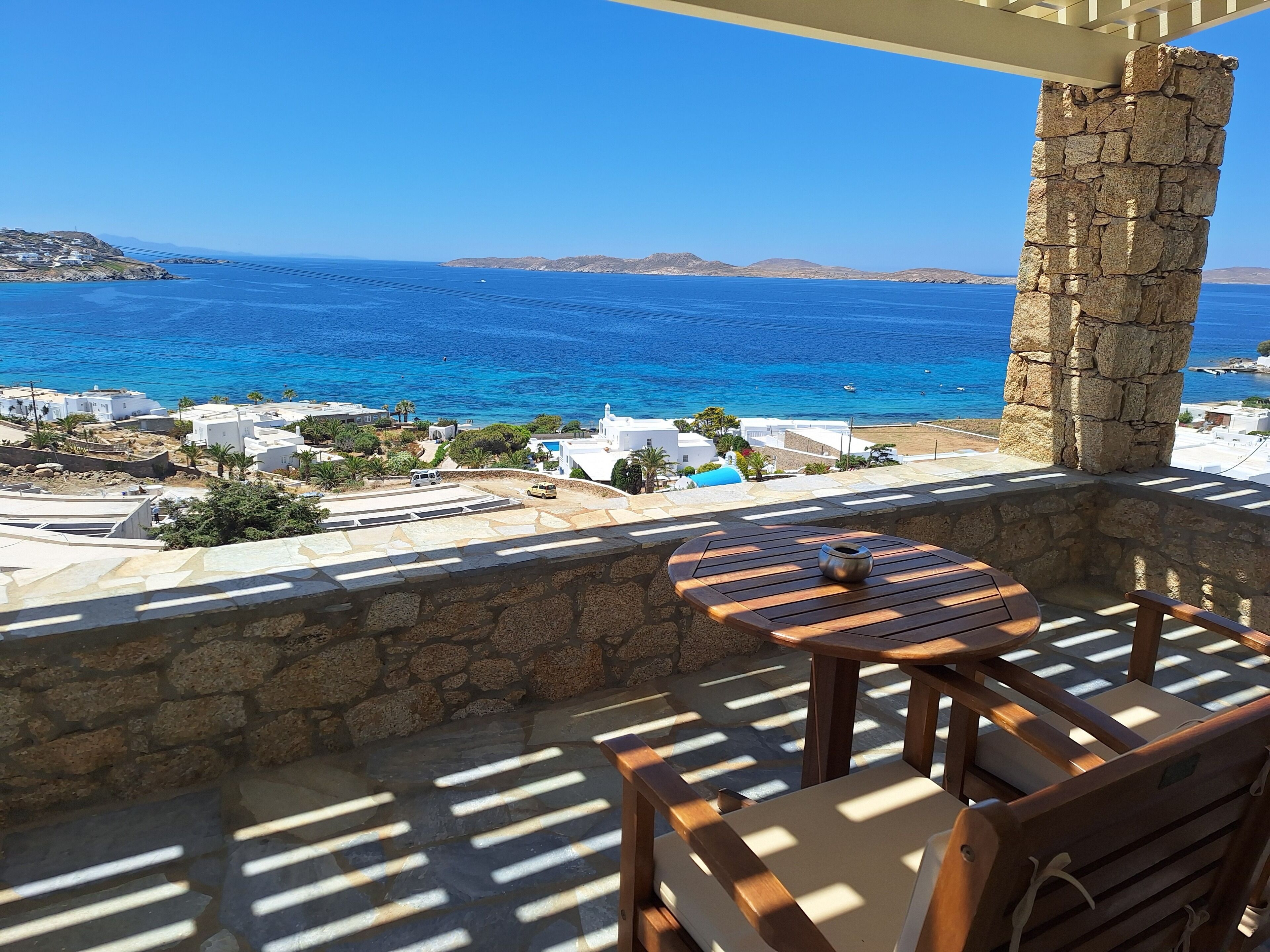 A balcony with a view of the sea, stone pillar, and a table with a cup.